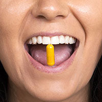 A person with an open mouth holding a yellow capsule on their tongue.