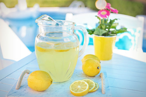 A pitcher of lemonade on a table surrounded by lemons.