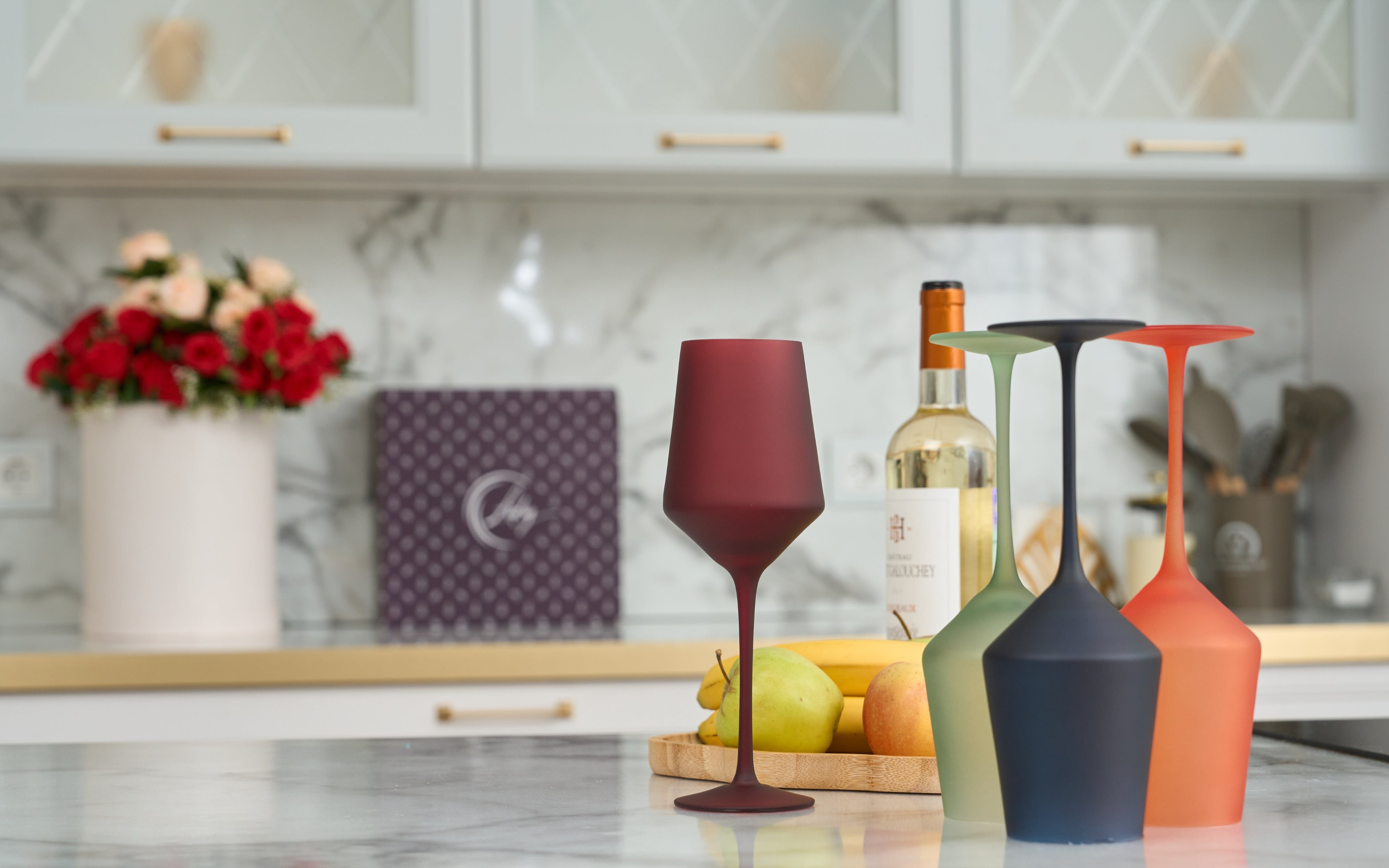 Modern frosted wine glasses and colorful decanters set on a chic kitchen counter.