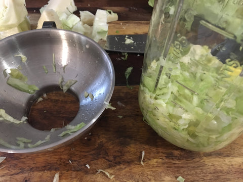 Stainless steel canning funnel and large mason jar full of cabbage for sauerkraut