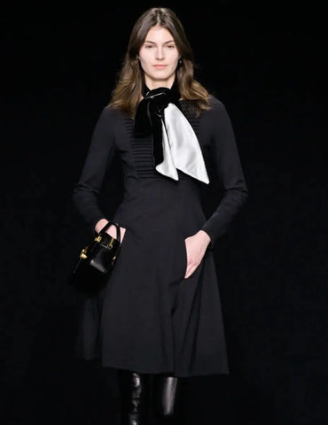 Model in a long-sleeve black midi dress with thigh-high boots and a black and white scarf tied around her neck