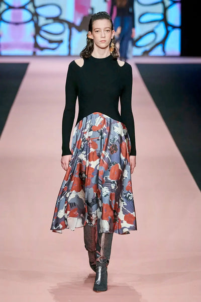 Model wearing cold shoulder cut black on top and colorful patterned below dress