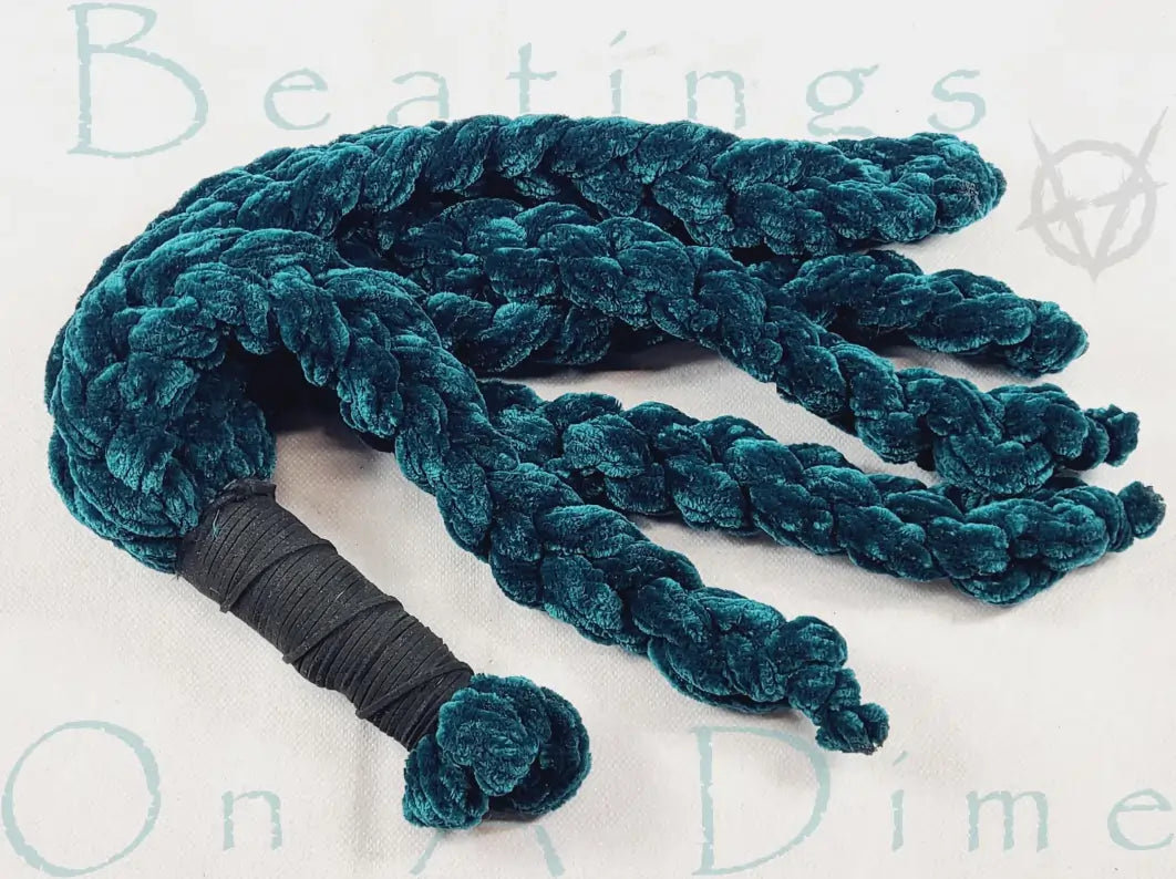 Blue velvet BDSM flogger with black wrapped handle, a plush impact play toy delivering soft thuddy sensations in flogging kink scenes.