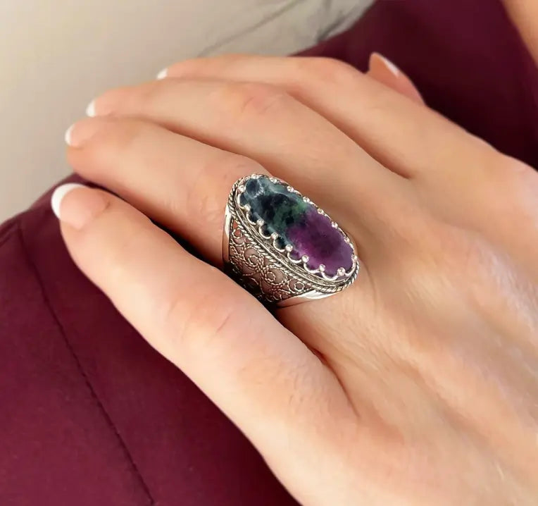 Hand wearing ornate silver ring with oval Ruby Zoisite gemstone, detailed crystal jewelry blending love and grounding energy.