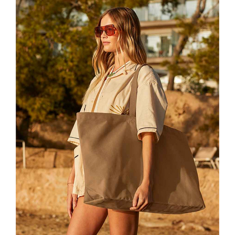 A model promoting a large brown tote bag without any print or branding.