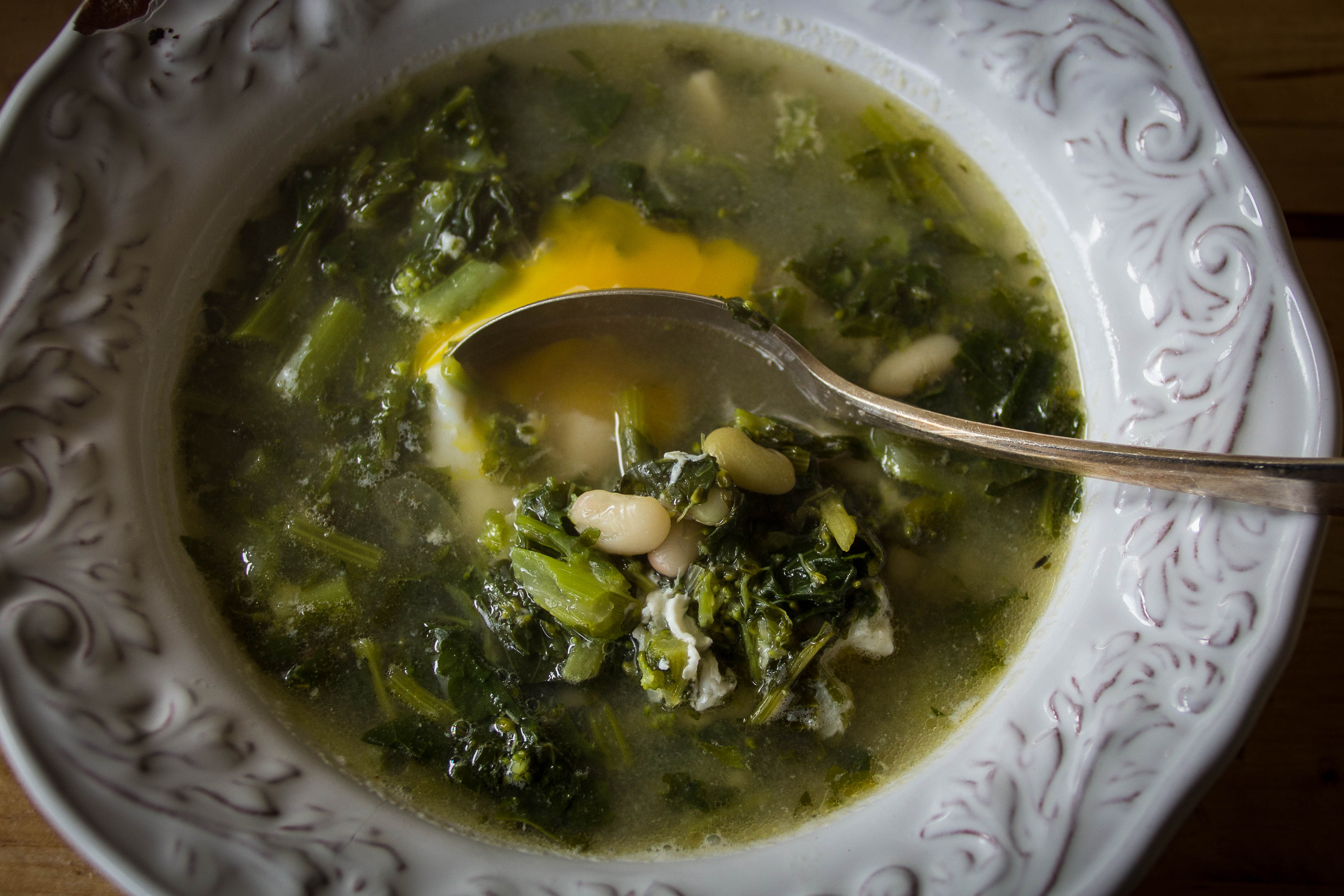 White bean and broccoli rabe soup in a bowl, topped with a poached egg