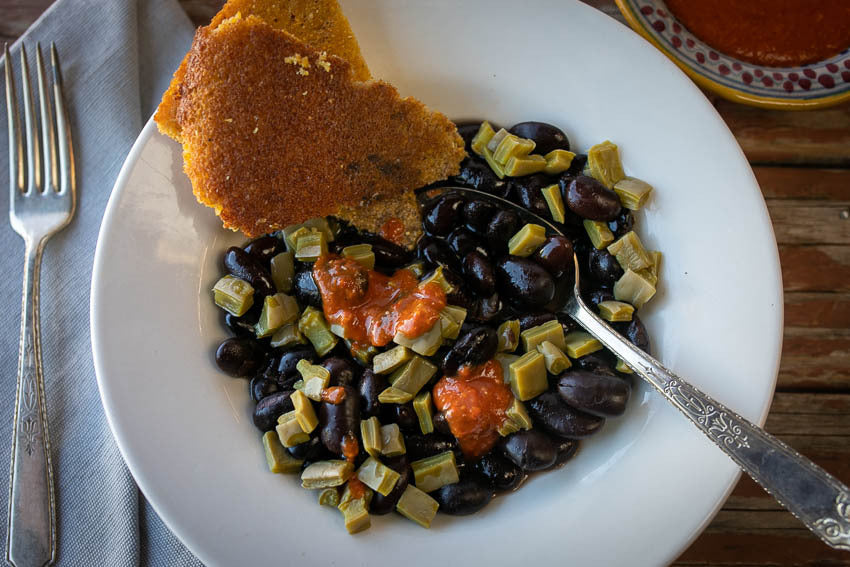 A serving bowl with cooked black beans, cooked cactus, salsa, and cornbread