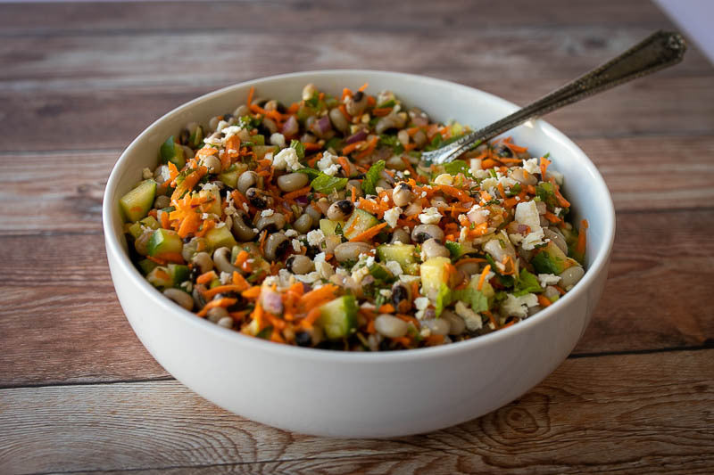 Black eyed pea salad with shredded carrots and cucumbers in a white serving bowl