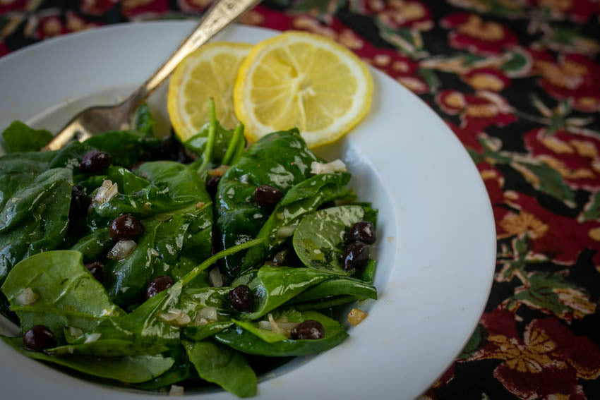 Baby spinach and black garbanzo salad in a white serving bowl