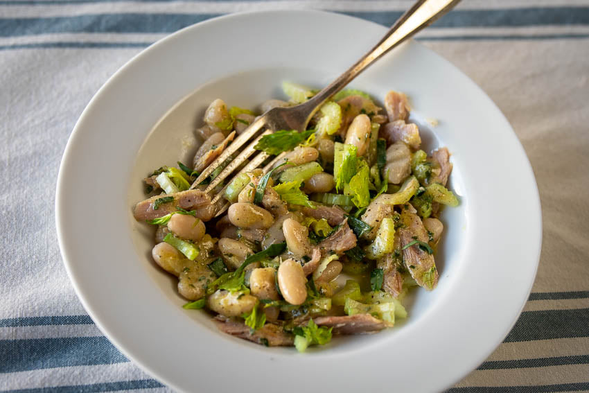 A medium bowl with white bean diced tarragon, celery and smoked trout