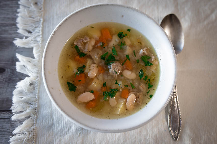 White bean, vegetable, and sausage stew served in a white bowl
