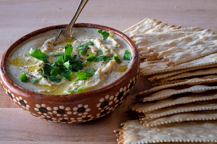 White bean spread with diced parsley as garnish, with crackers next to the bowl 