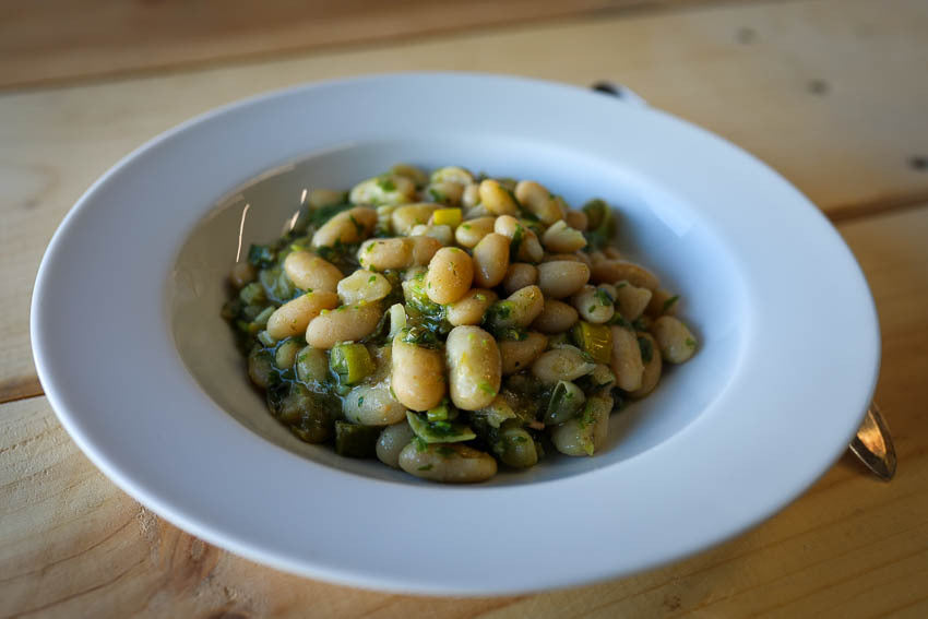 Cooked white Marcella beans in a serving bowl with leeks and parsley pistou