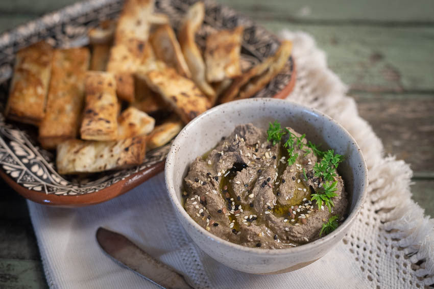 Black garbanzo hummus in a bowl with toasted pita chips.