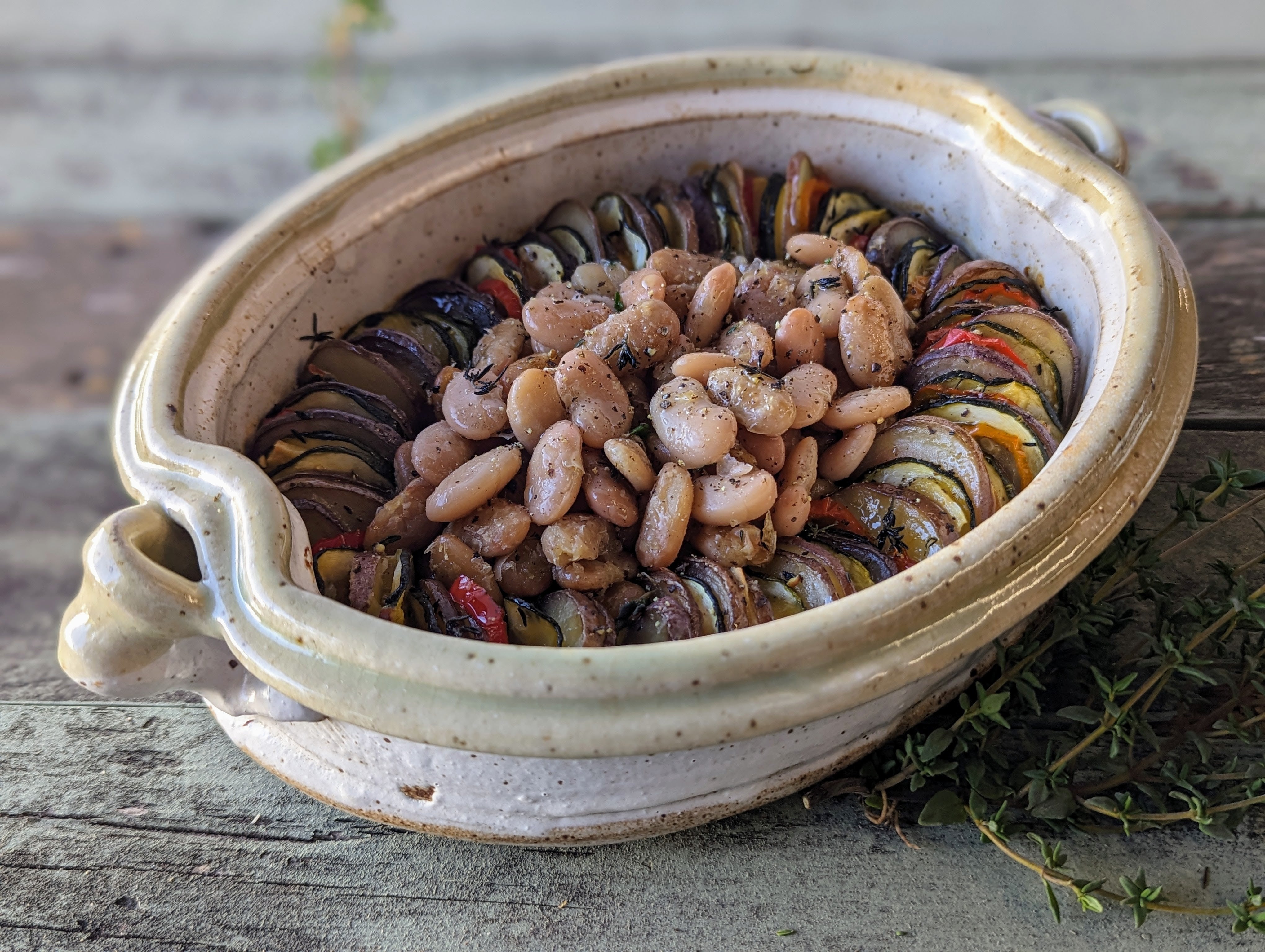 A layered tian of potatoes, zucchini, and bell pepper with white beans in the center