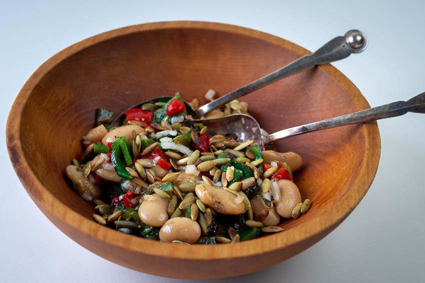 Cooked heirloom white beans and roasted red and green peppers, topped with pumpkin seeds, in a wooden salad bowl