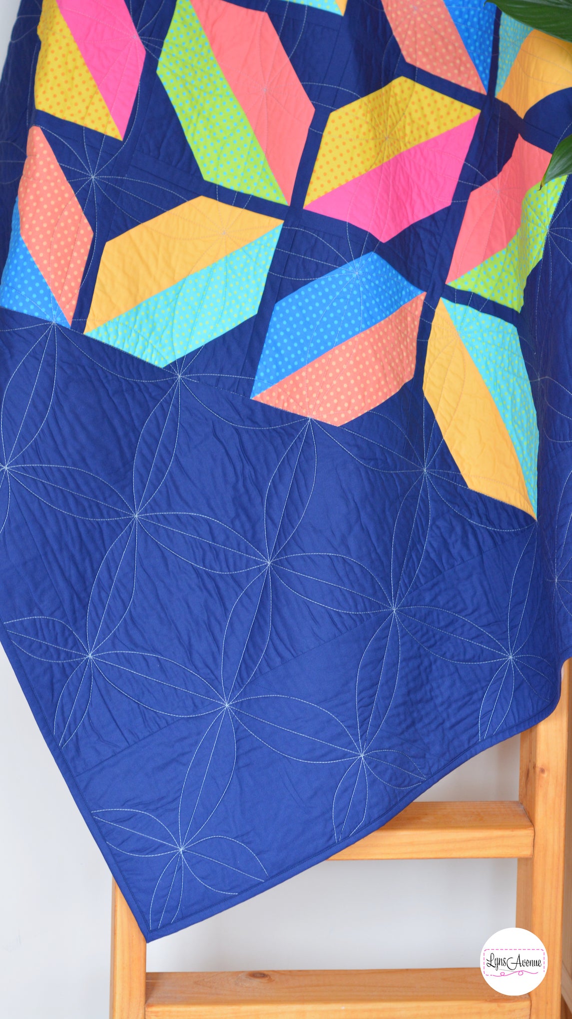 Flourishing Quilt pattern - a flower design quilt pattern in bright pink, yellow, blue and peach colour on a navy blue background draped on a quilt ladder