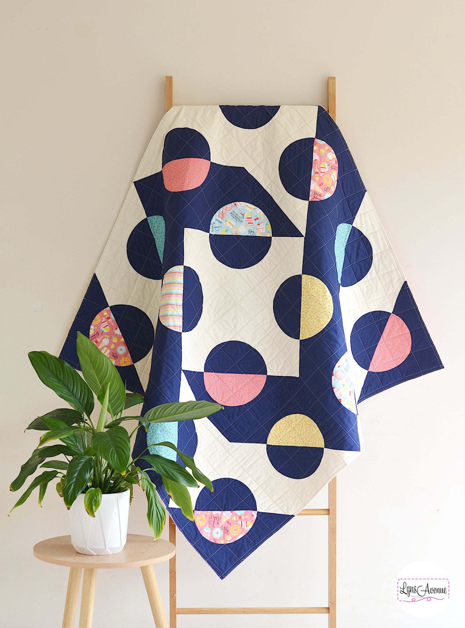 Hook and Pop quilt in navy blue and cream background with pops of colour in yellow, pink, green fabrics with sprinkles and ice cream designs on a quilt ladder