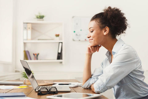 Smiling Brown-Skinned Woman Seated at Desk with Laptop.