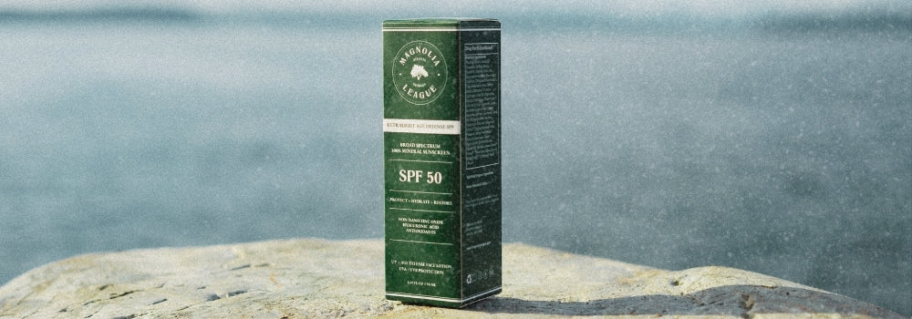 Magnolia League mineral sunscreen green product box on rock beside ocean