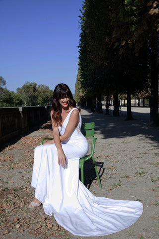 Bride wearing white wedding dress while sitting in chair in park.