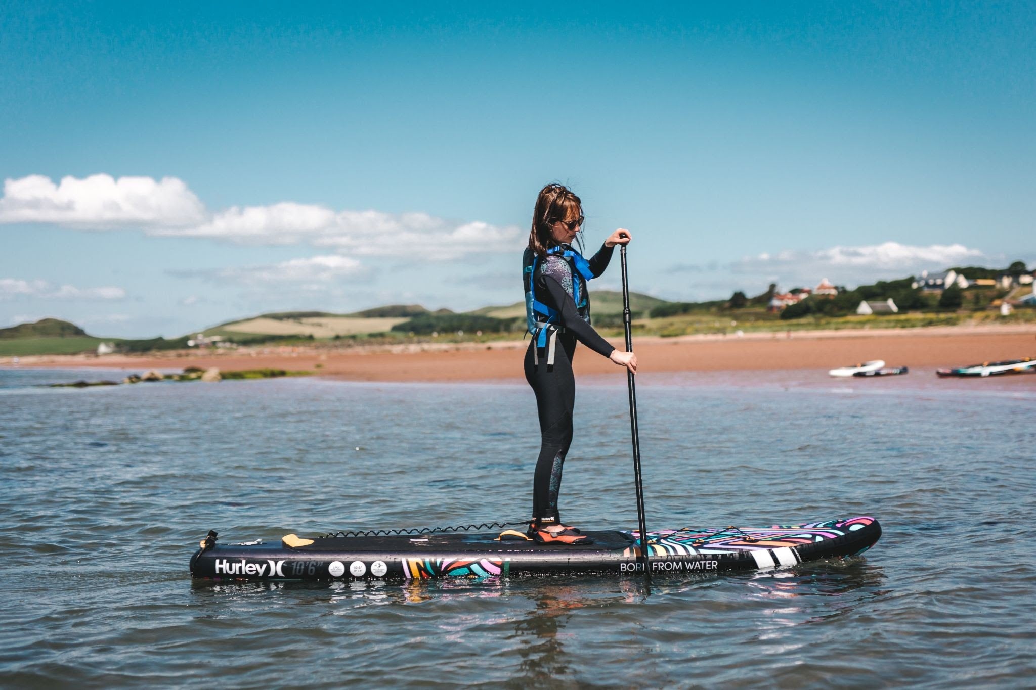 A woman paddle boarding at the beach on a Hurley Phantomtour Colorwave SUP