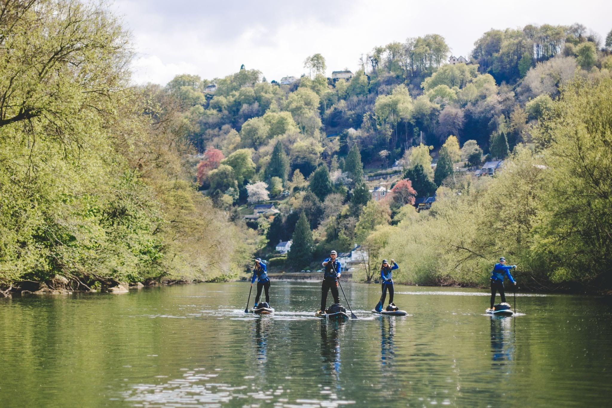 four people paddle boarding towards the camera on a river