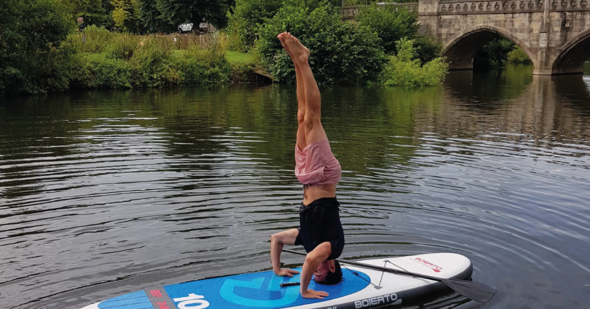 A person doing a headstand on a paddle board
