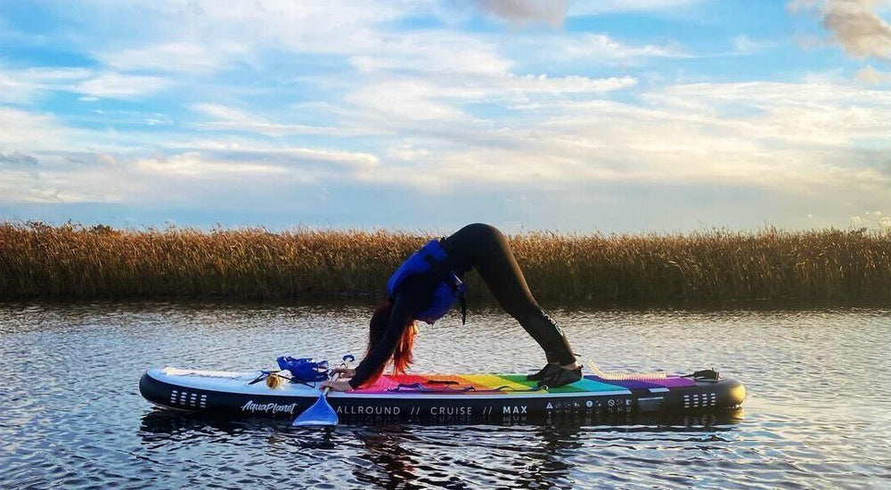 A person performing a downward dog yoga pose on a Aquaplanet MAX rainbow paddle board