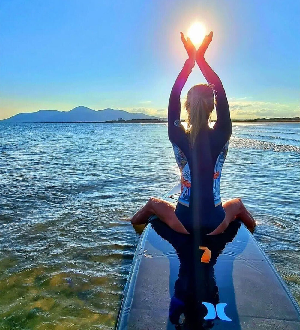A woman sitting on a Hurley paddle board with hands above her head in a peaceful pose