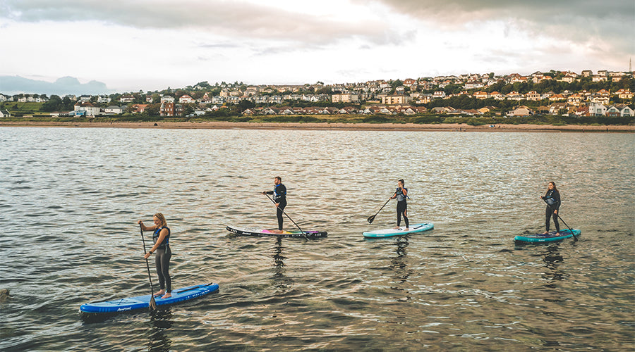4 people paddle boarding in calm waters