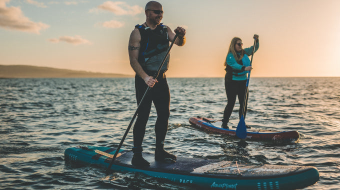 Two people on Aquaplanet paddle boards wearing buoyancy aids and ankle leashes.