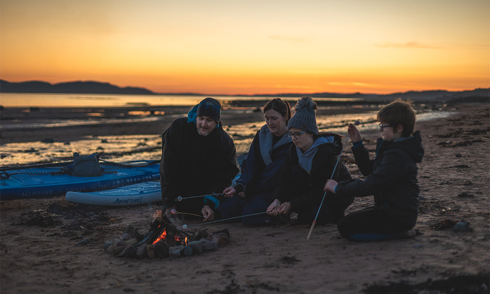 A family on the beach with a campfire and paddle boards