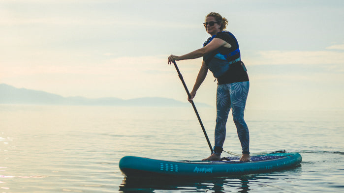 A woman wearing leggings and a t-shirt under her buoyancy aid on an Aquaplanet PACE teal paddle board
