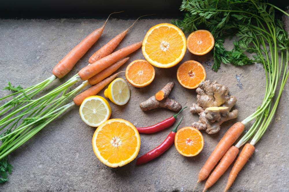 Picture of citrus fruits, turmeric and carrots on a gray surface.