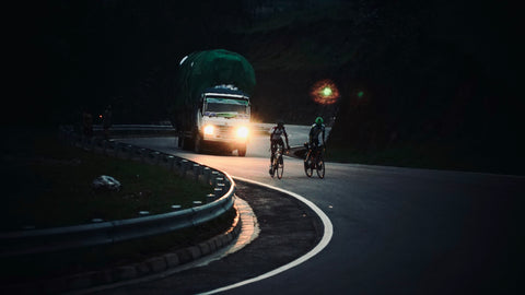 two cyclists riding on the road infront of a truck