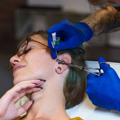 piercer performing a tragus piercing with a needle.