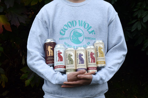 man wearing good wolf sweatshirt holding a variety of good wolf probiotic refreshers