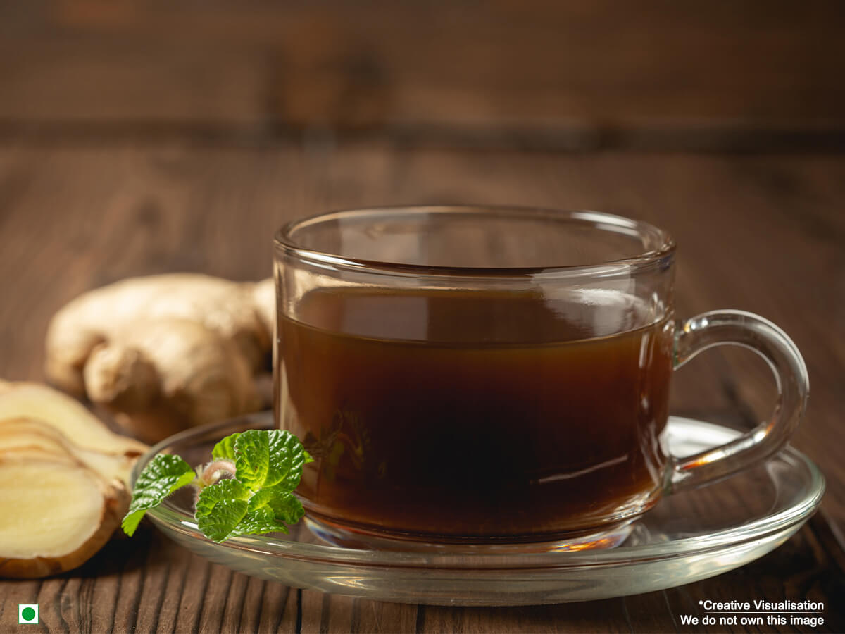  A cup of ginger tea is kept on a wooden table with cut slices of ginger beside it.