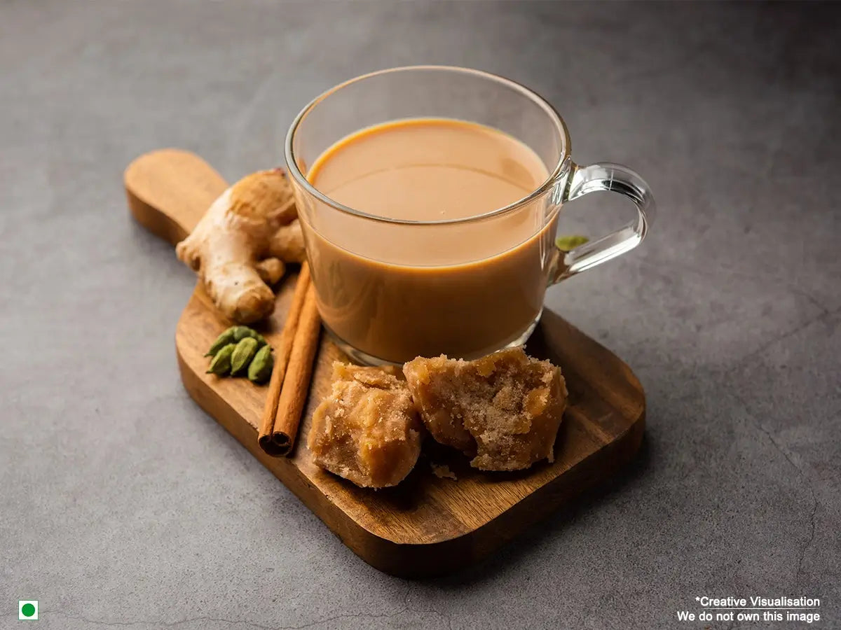 An image of ginger tea placed on a table with ginger slices and jaggery on the side.