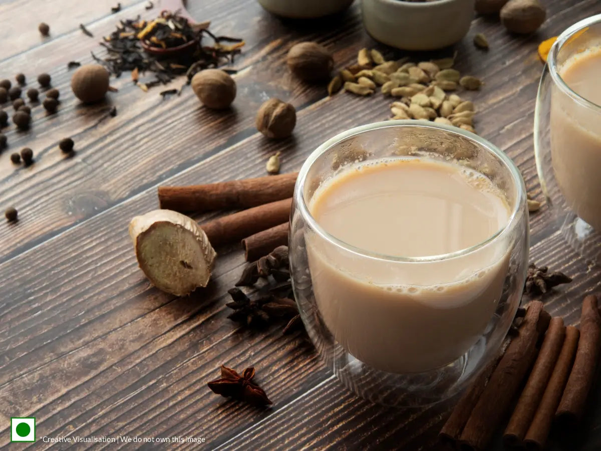 An image of masala chai placed on a wooden table beside spices like cardamom, ginger and cinnamon.