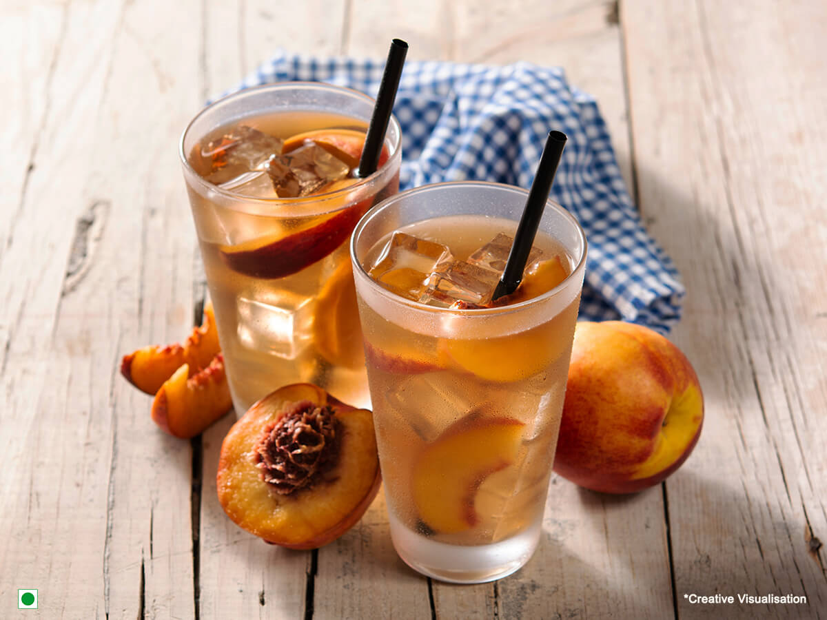 A tall glass of peach ice tea filled with ice cubes and slices of peach inside!