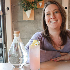 Freeland Spirits Bar Manager Summer posing with her cocktail I Ca Buy Myself Flowers and bottle of Dry Gin