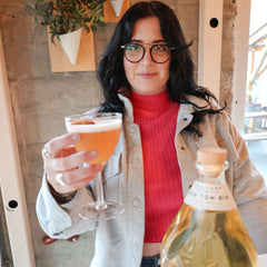 Elaine posing with The Georgia Poppy cocktail and bottle of Freeland Old Tom Gin