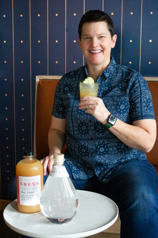 Beach Pace, CEO of Big Brothers Big Sisters Columbia NW. Freeland Spirits Q4 Free Spirit, 2023. Smiling with a Free Fallin' cocktail next to a bottle of Freeland Dry Gin.