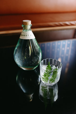 Freeland Spirits Forest Gin green bottle in tasting room next to Forest Negroni garnished with fern sprigs