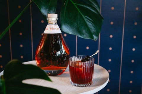 Bottle of Freeland Rye next to Cherry Vieux Carre cocktail, surrounded by large tropical plant leaves.