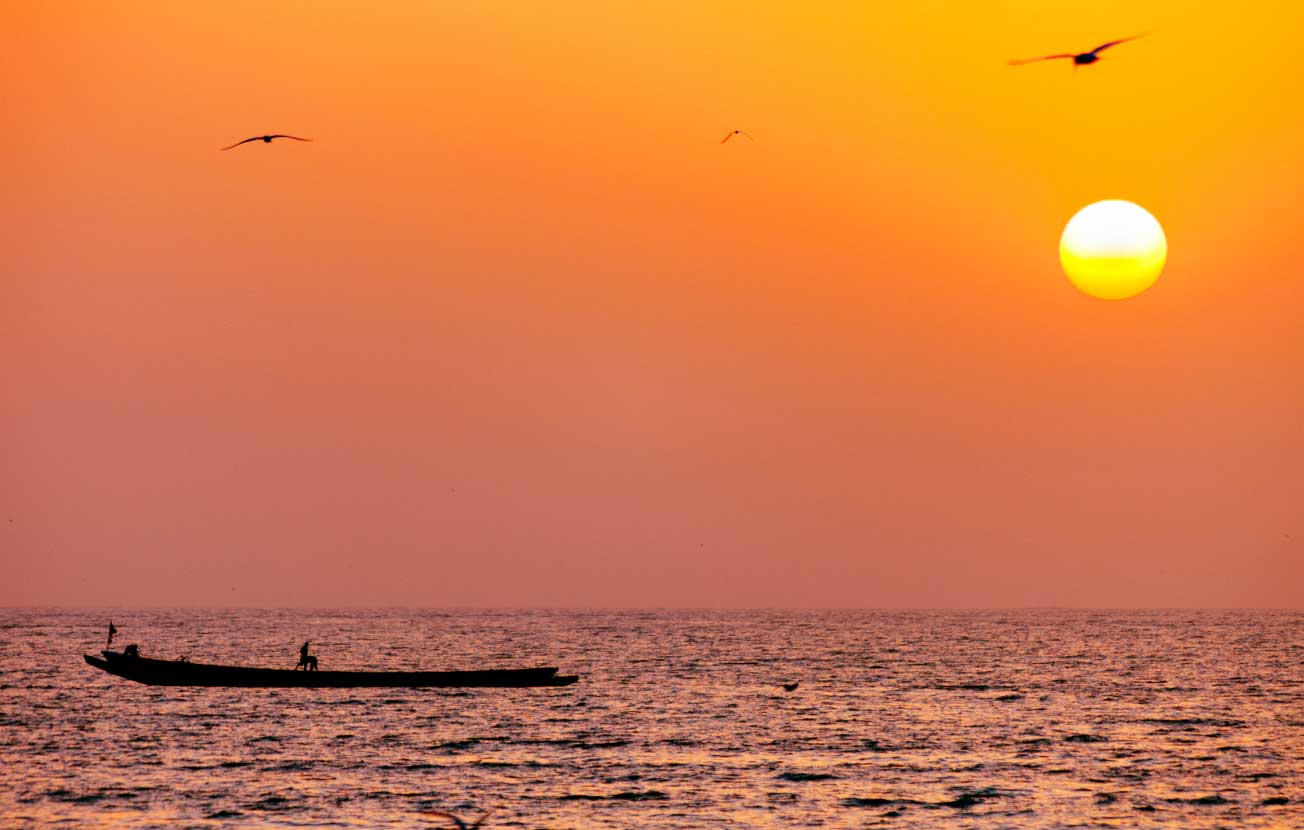 Alt: A sunset out at sea with an artisanal fishing boat in the foreground.