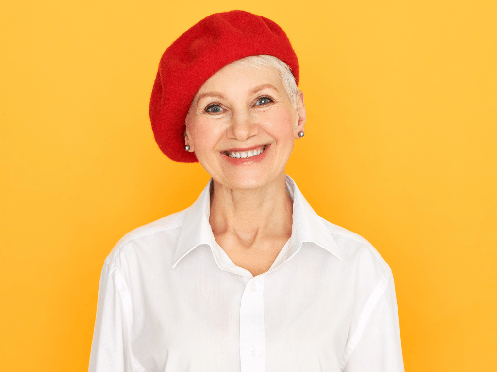 femme âgée souriante avec les cheveux courts portant bonnet rouge et une chemise blanche