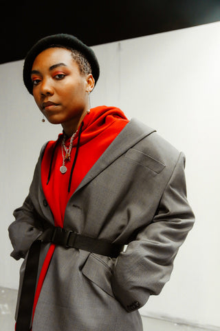 femme noir portant un béret noir sur la tête avec un pull rouge et une veste grise